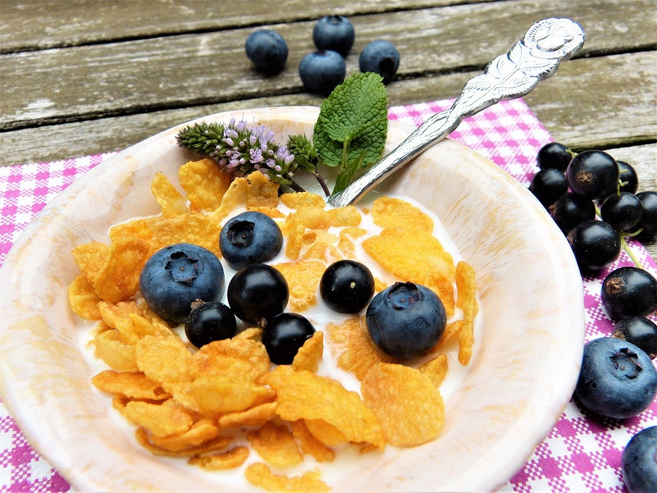 photo of a bowl of cornflakes with blueberries and a sprig of mint 