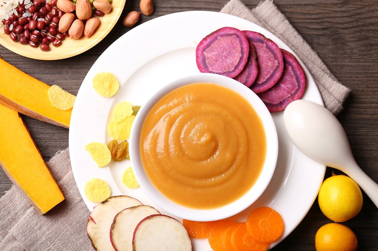 photo of a bowl of squash puree on a plate surrounded by sliced vegetables and fruits