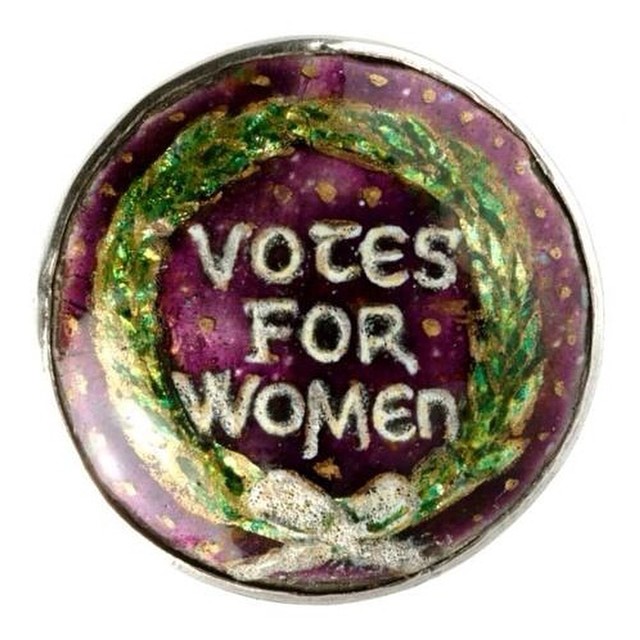 Shiny purple and green button with the words VOTES FOR WOMEN in silver lettering