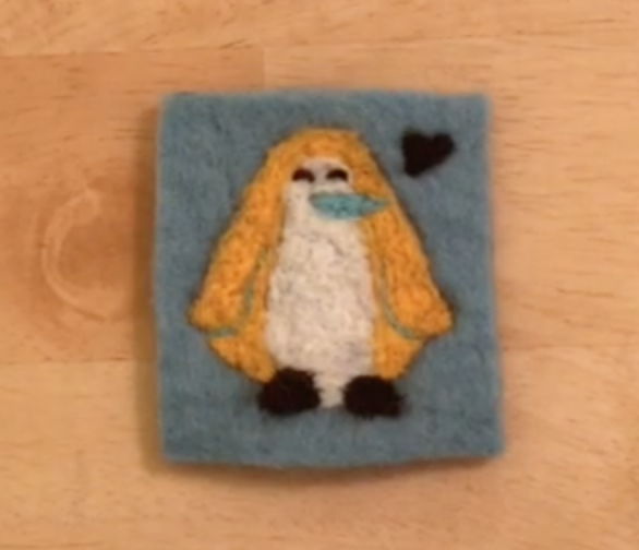 Felted penguin with yellow wings on a blue background with a small felted heart by its head