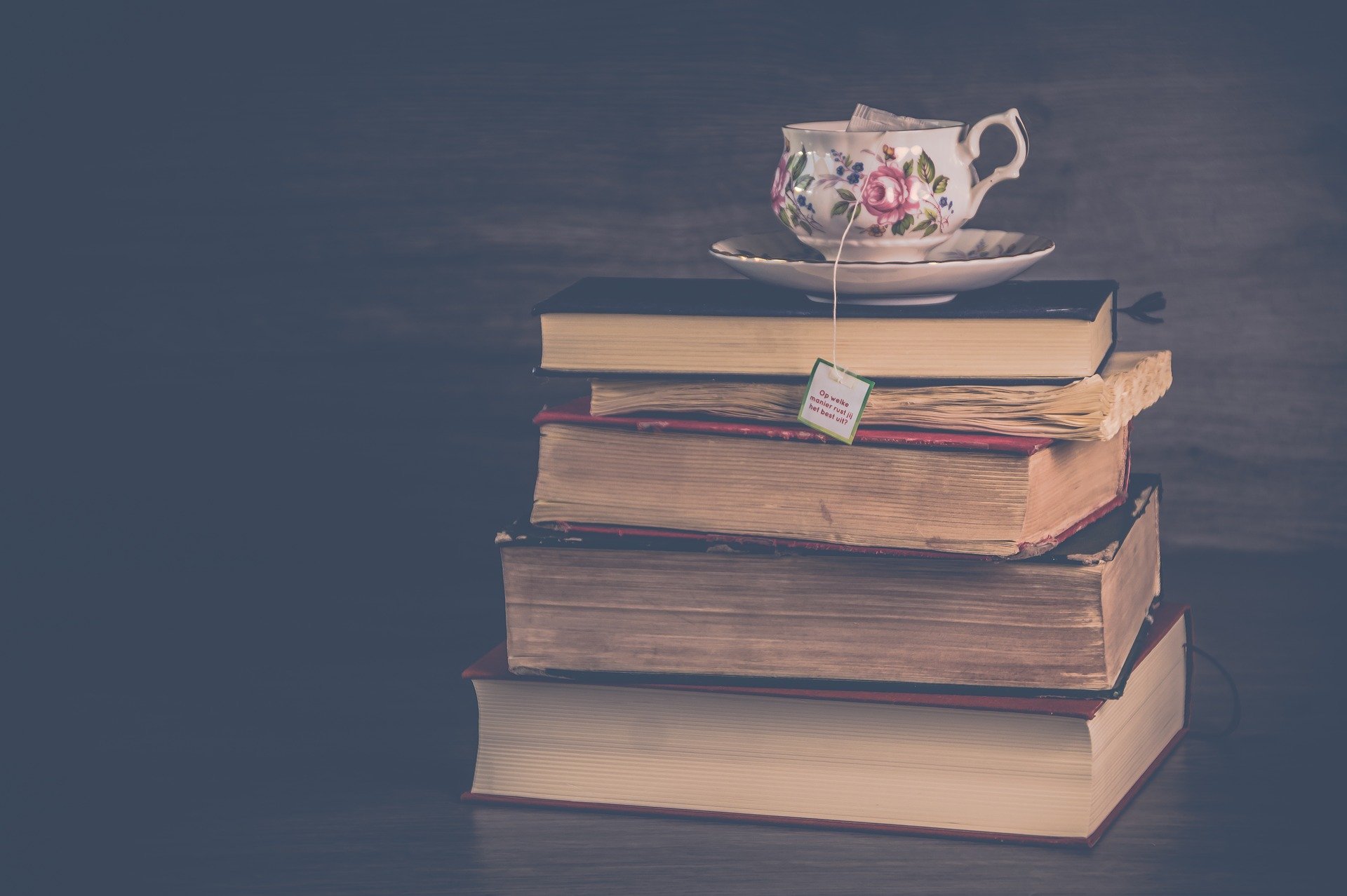 a pile of old books with a teacup sitting on top