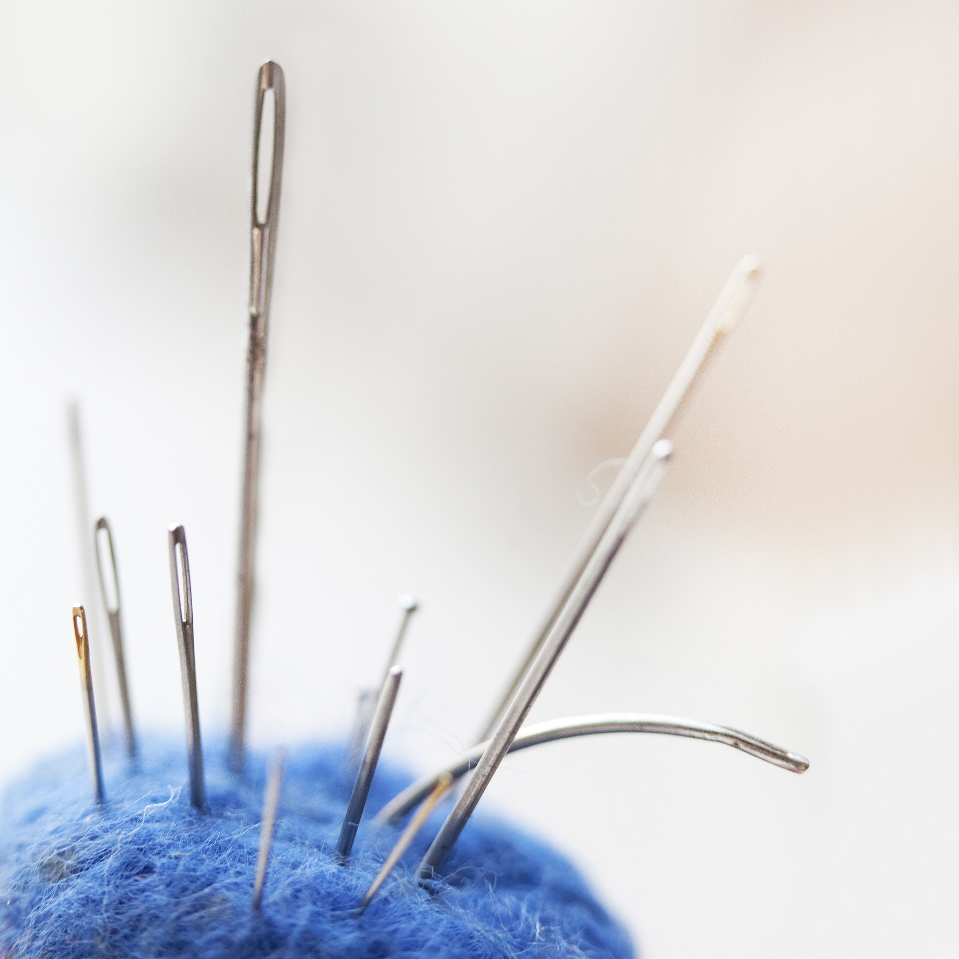 variety of sewing needles sticking out of the top of a blue ball of fuzzy yarn
