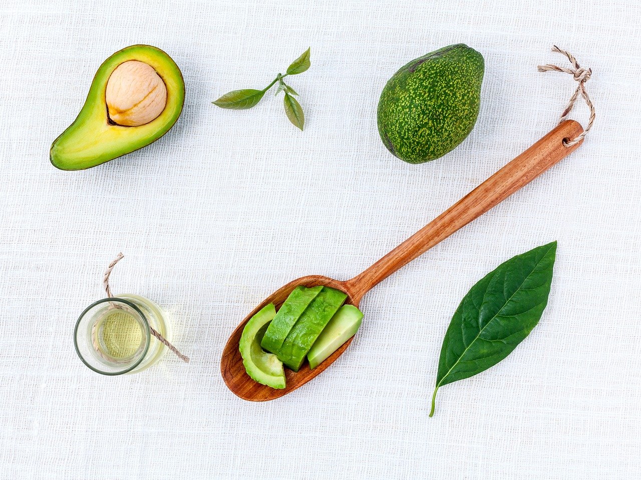 overhead angle photo of avocado, oil and herbs with a wooden spoon