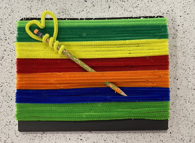 Notebook covered with multicolored pipe cleaners and decorated pencil