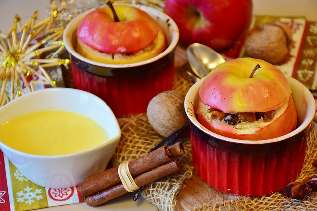 This image shows a place setting with cinnamon sticks, walnuts, a saucer with a yellow liquid, and two ramekins filled with baked apples.