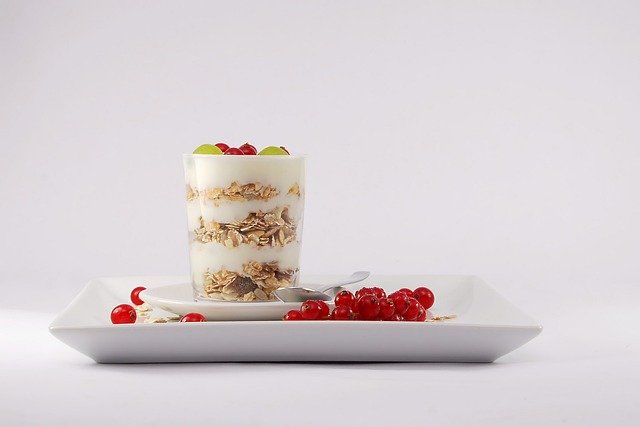 This image shows a rectangular plate with cranberries and a a cup of granola and fruit parfait with a spoon laid next to it.
