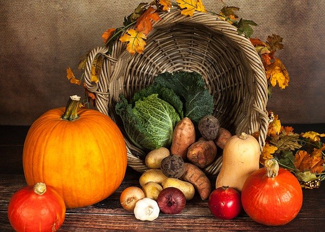 This image shows a variety of vegetables and fruits including pumpkins, tomatoes, garlic, potatoes, pomegranates, and lettuce in a basket outlined by imitation orange and yellow leaves.