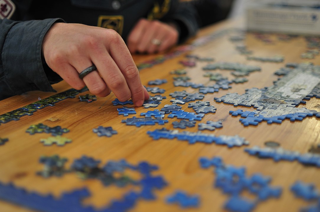 A person's hands working on a jigsaw puzzle on a wooden table