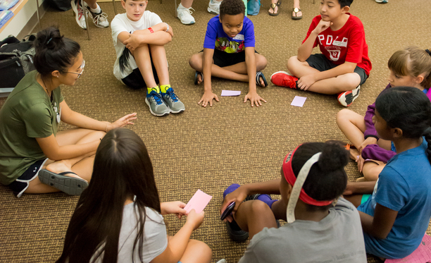 group of teens sitting on the floor in a circle and talking