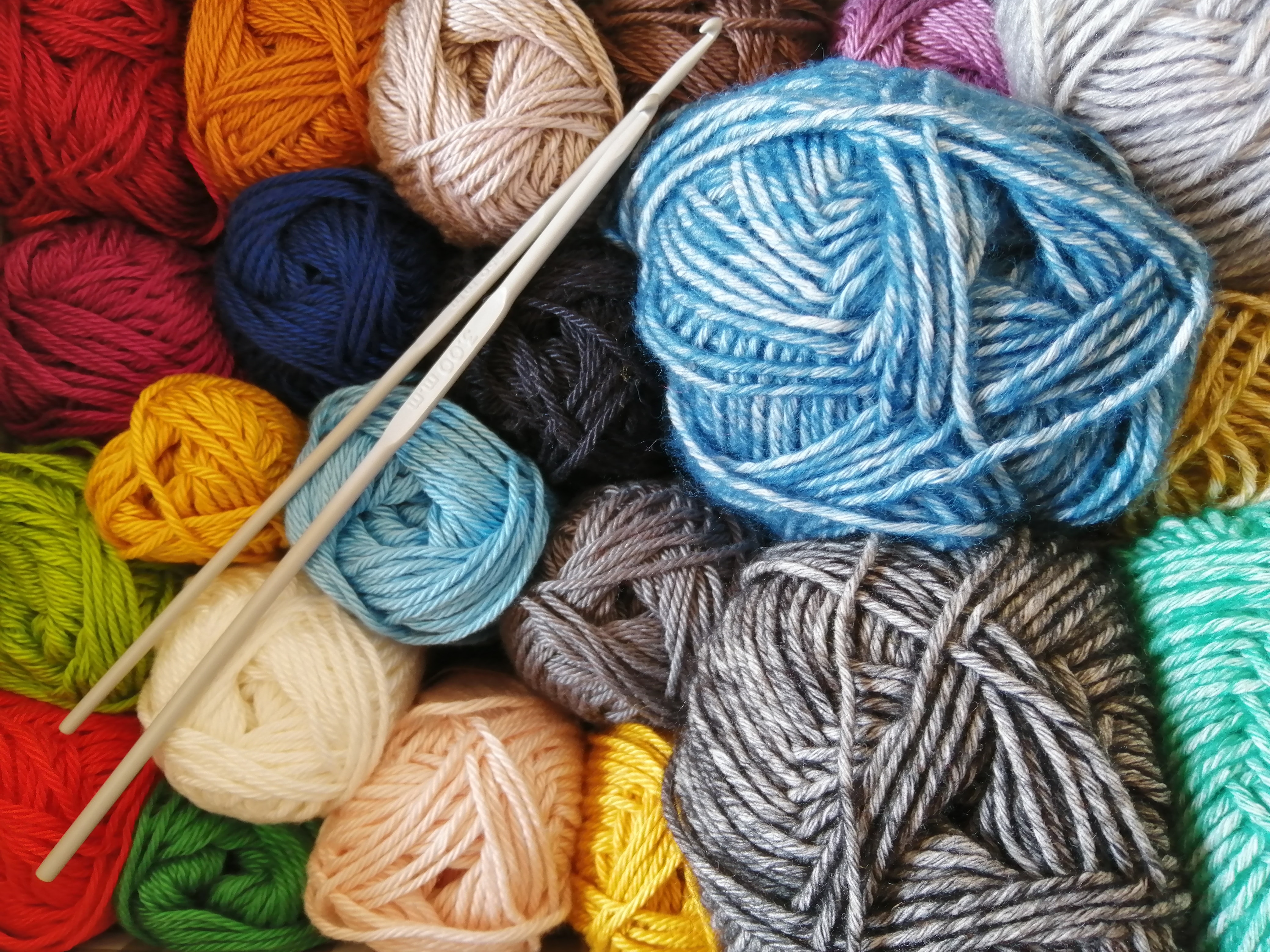 colorful balls of yarn with two gray crochet hooks on top