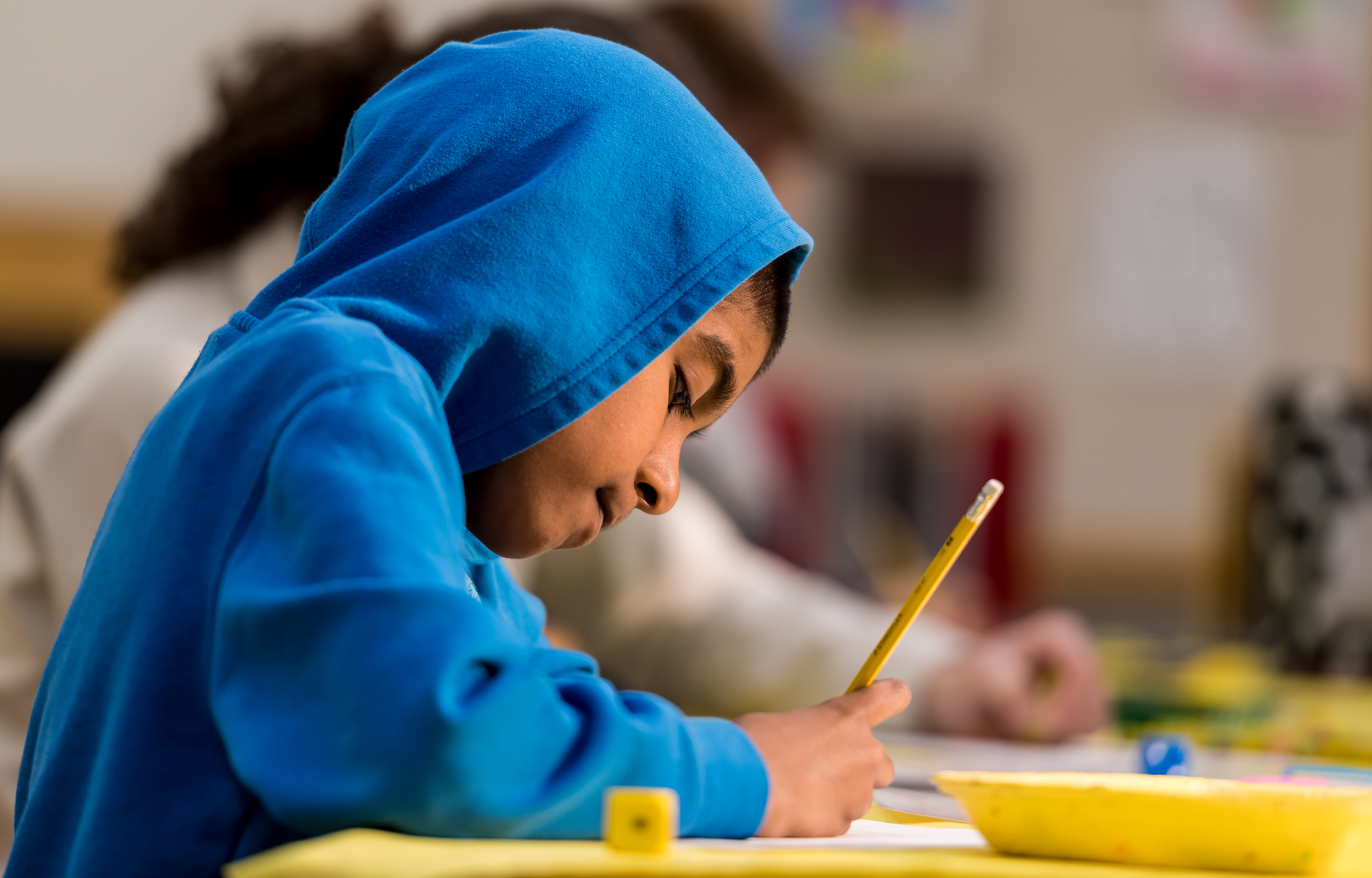 young teen wearing a blue hoodie sweatshirt and writing with a pencil