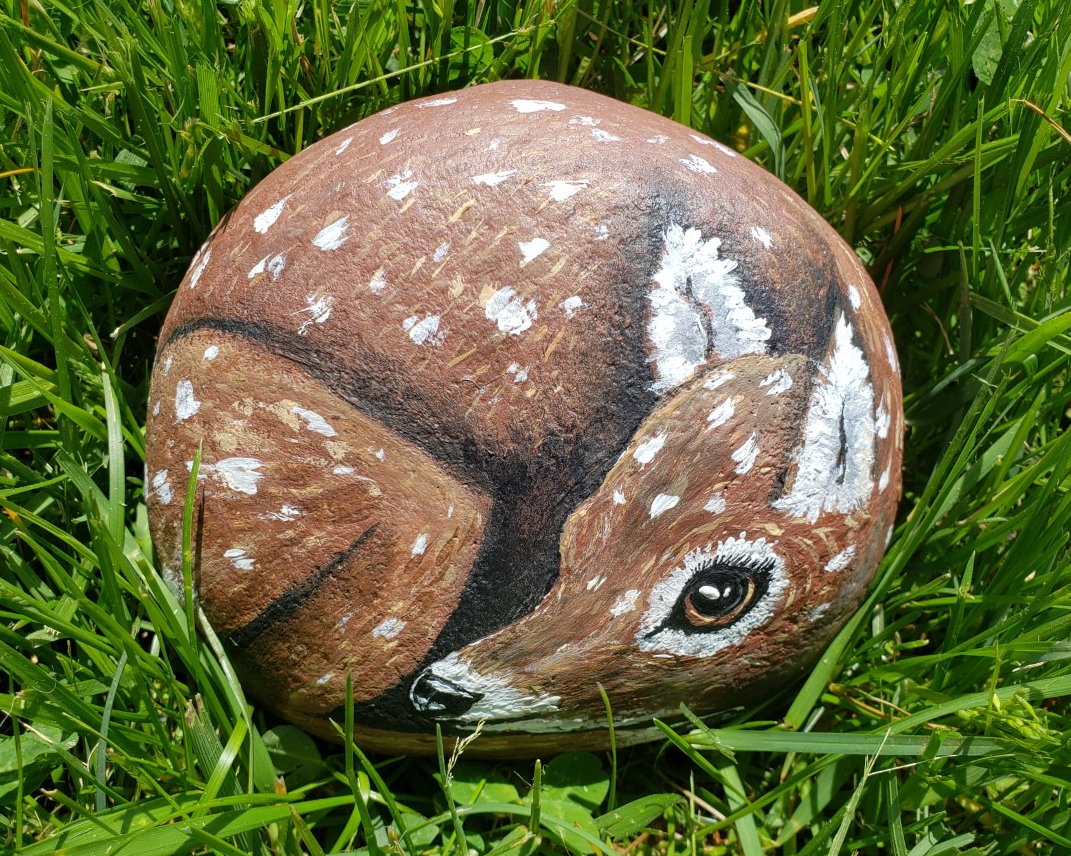 a rock painted to look like a deer sitting in the grass