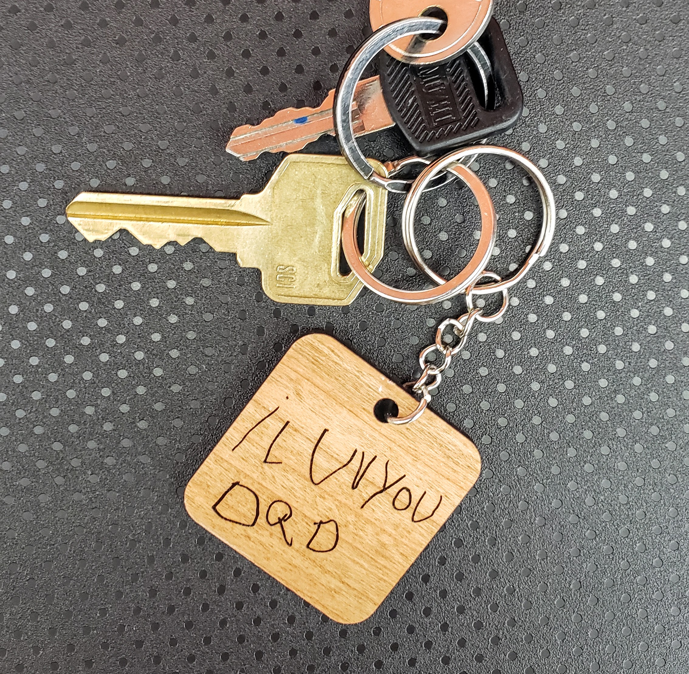 Wooden keychain with the phrase "I luv you dad" (sic) on a black background