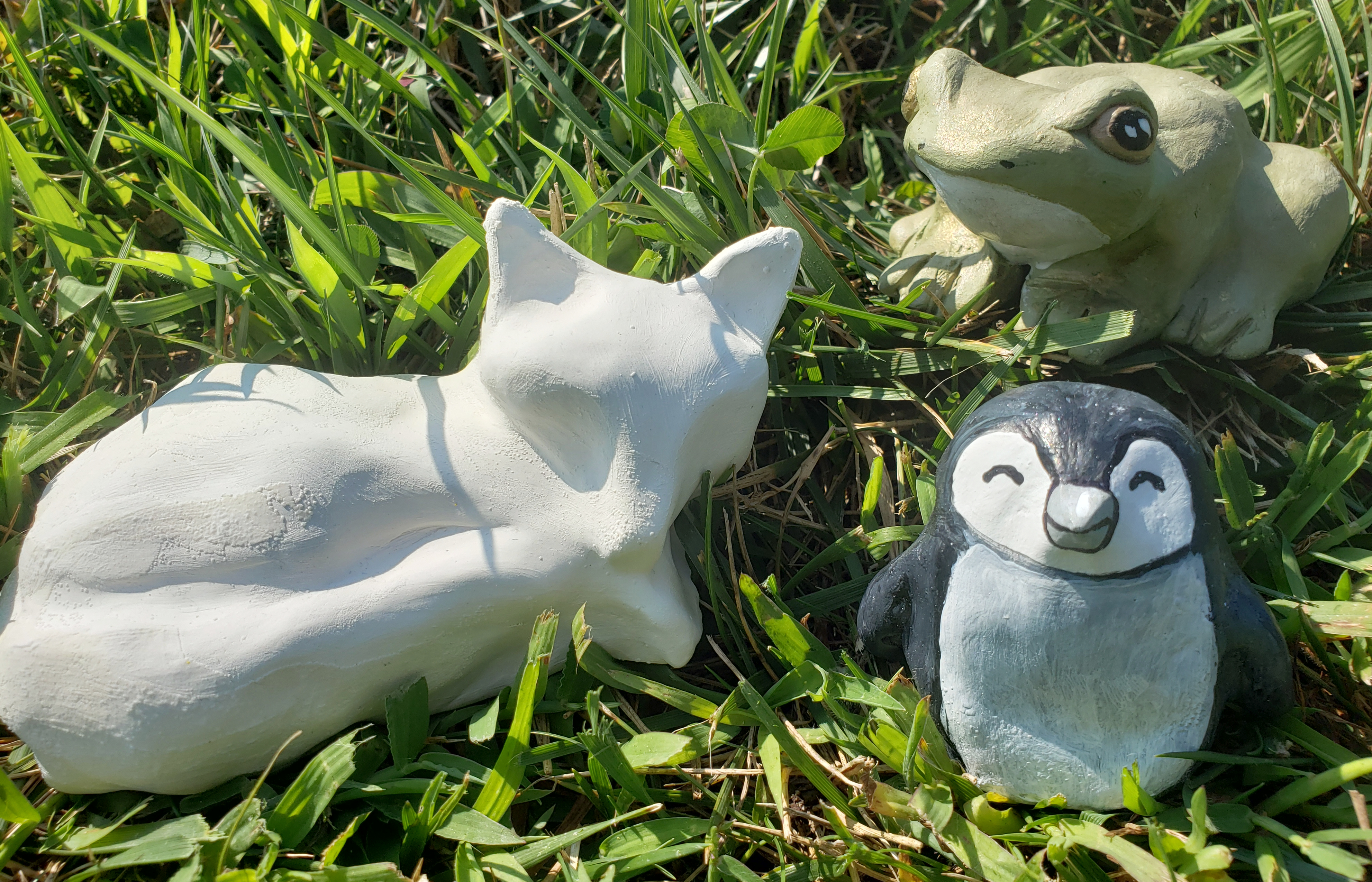 a fox frog and penguin made of air dry clay sitting in the grass