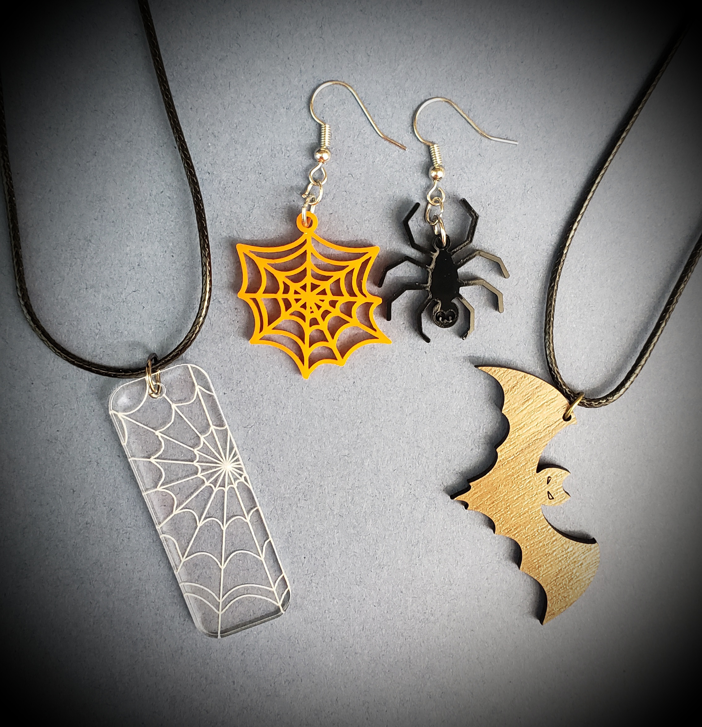 Spiderweb, bat, and spider jewelry pieces shown against blue background