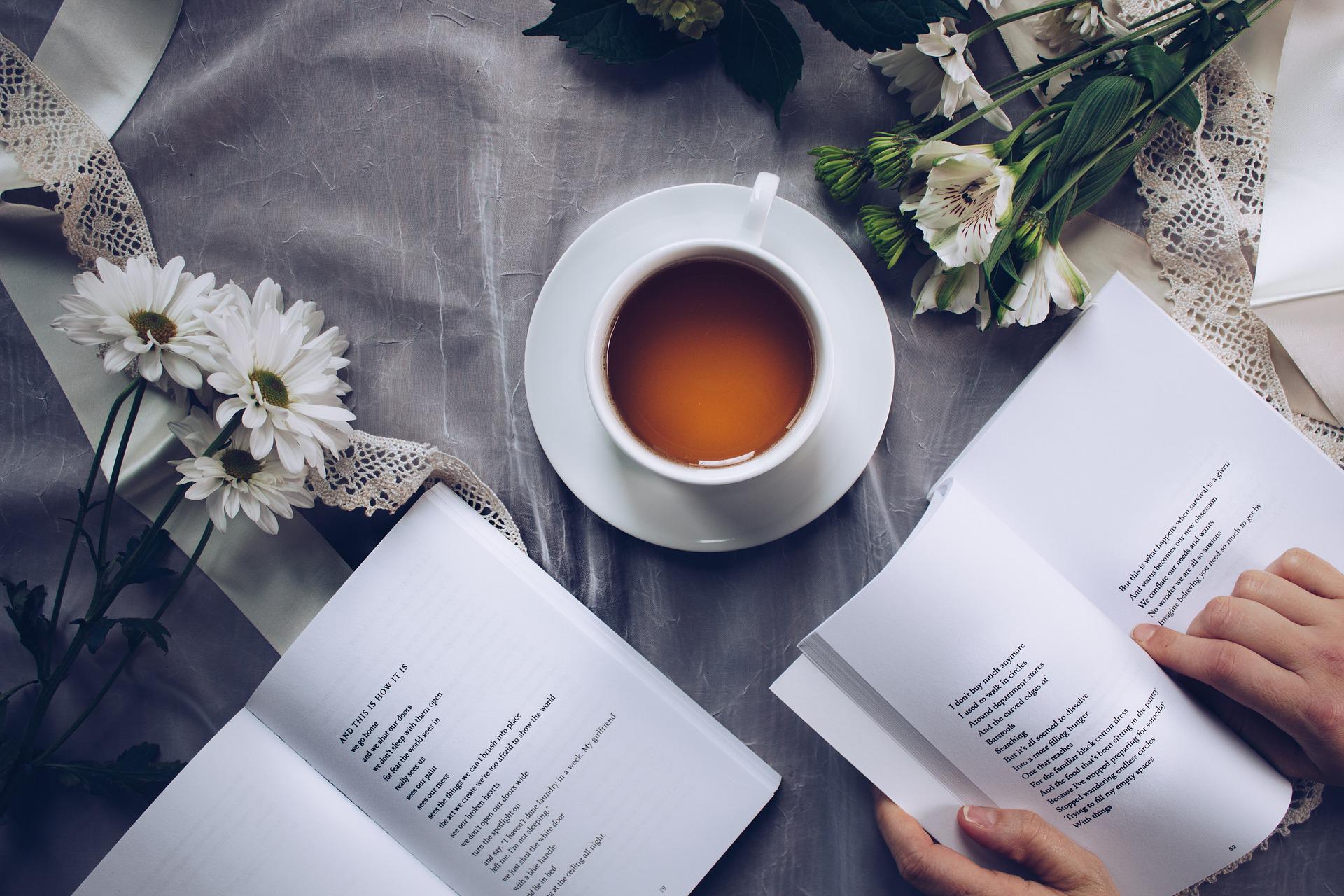 two open books with a cup of tea on a table with white tablecloth