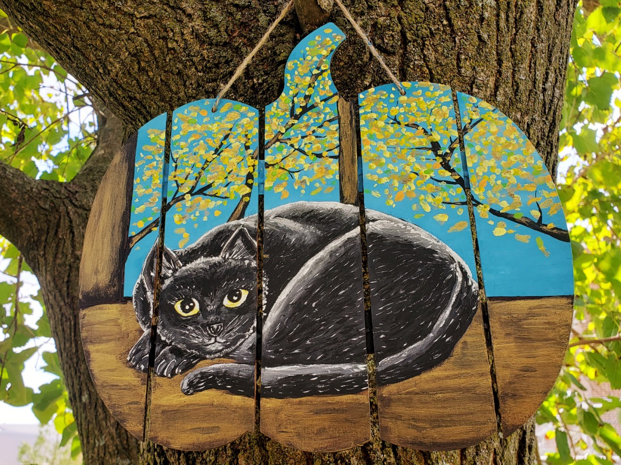 a wood plank sign shaped like a pumpkin with a painted cat on it
