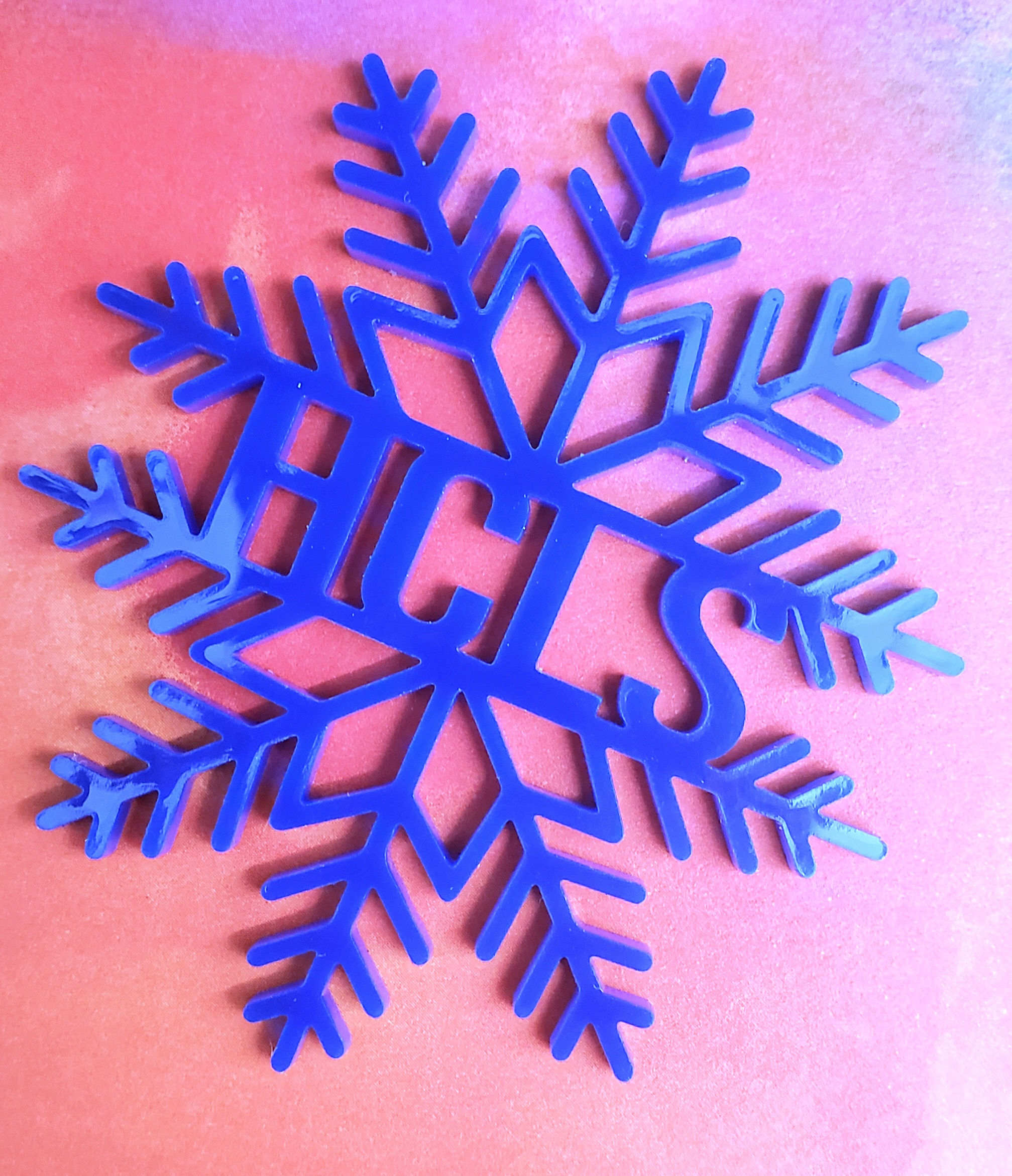 Blue Acrylic Snowflake with HCLS words cut out shown on pink  background