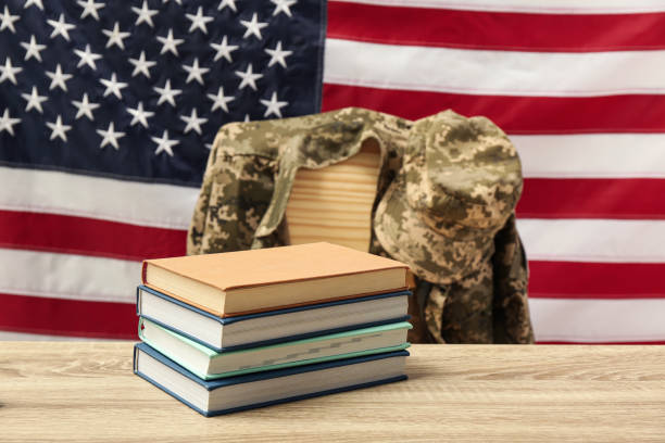 american flag background, with a pile of books in front and a camo jacket draped over a chair