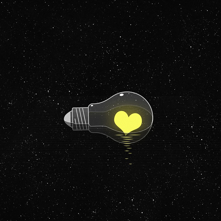 yellow heart inside clear light bulb with black background