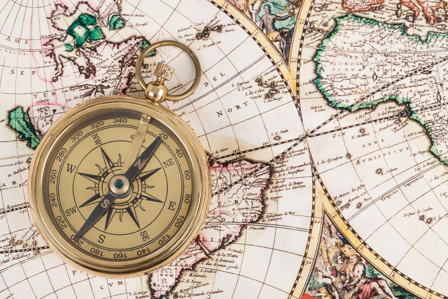 Gold compass laying on top of an antique map displaying the world. 