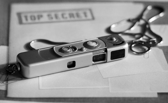 The image depicts an old-school spy camera, a monocle, and a folder labeled "top secret."