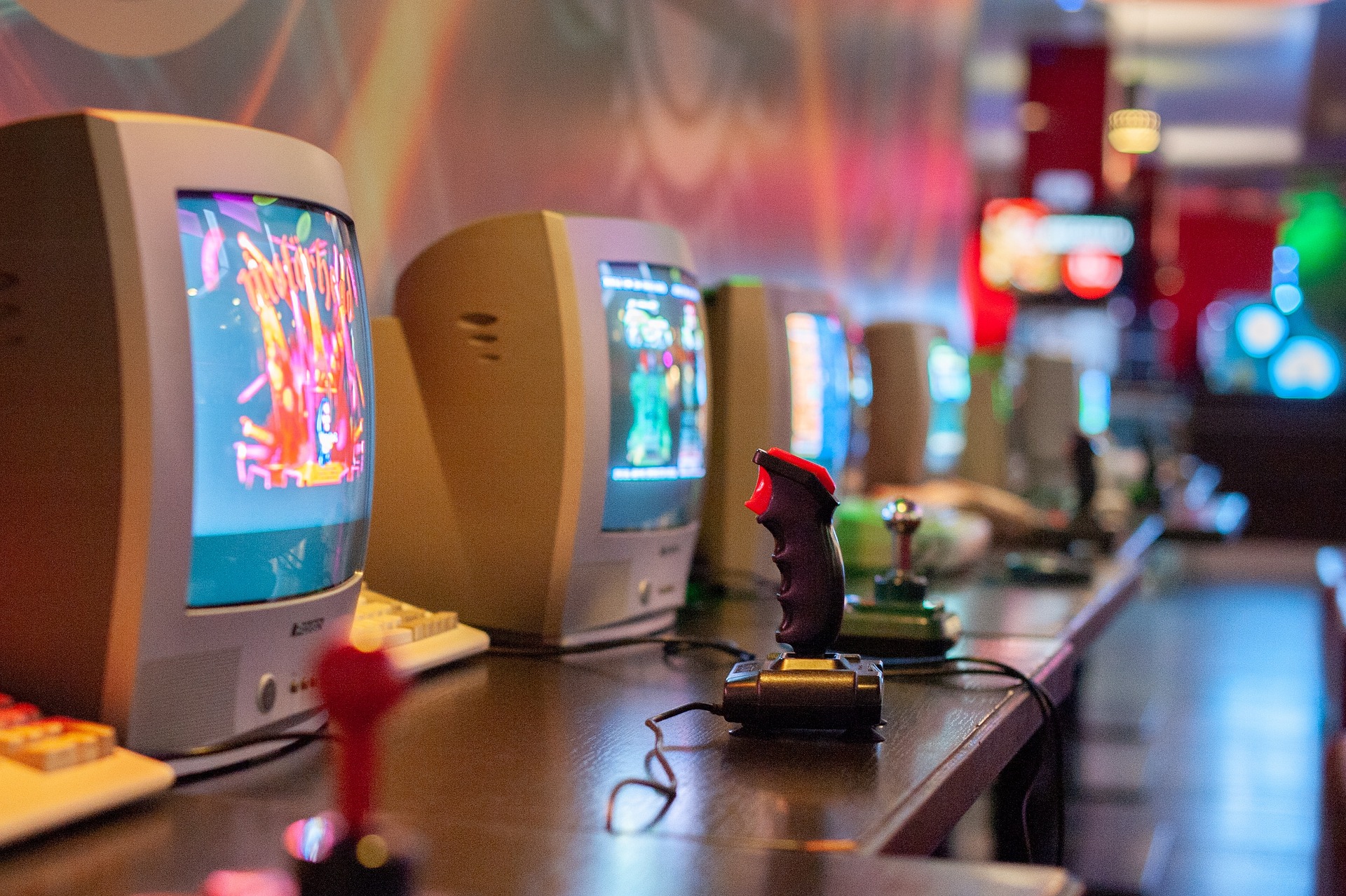 CRT TV screens with old gaming joysticks set up along a wooden desk, with retro video games running