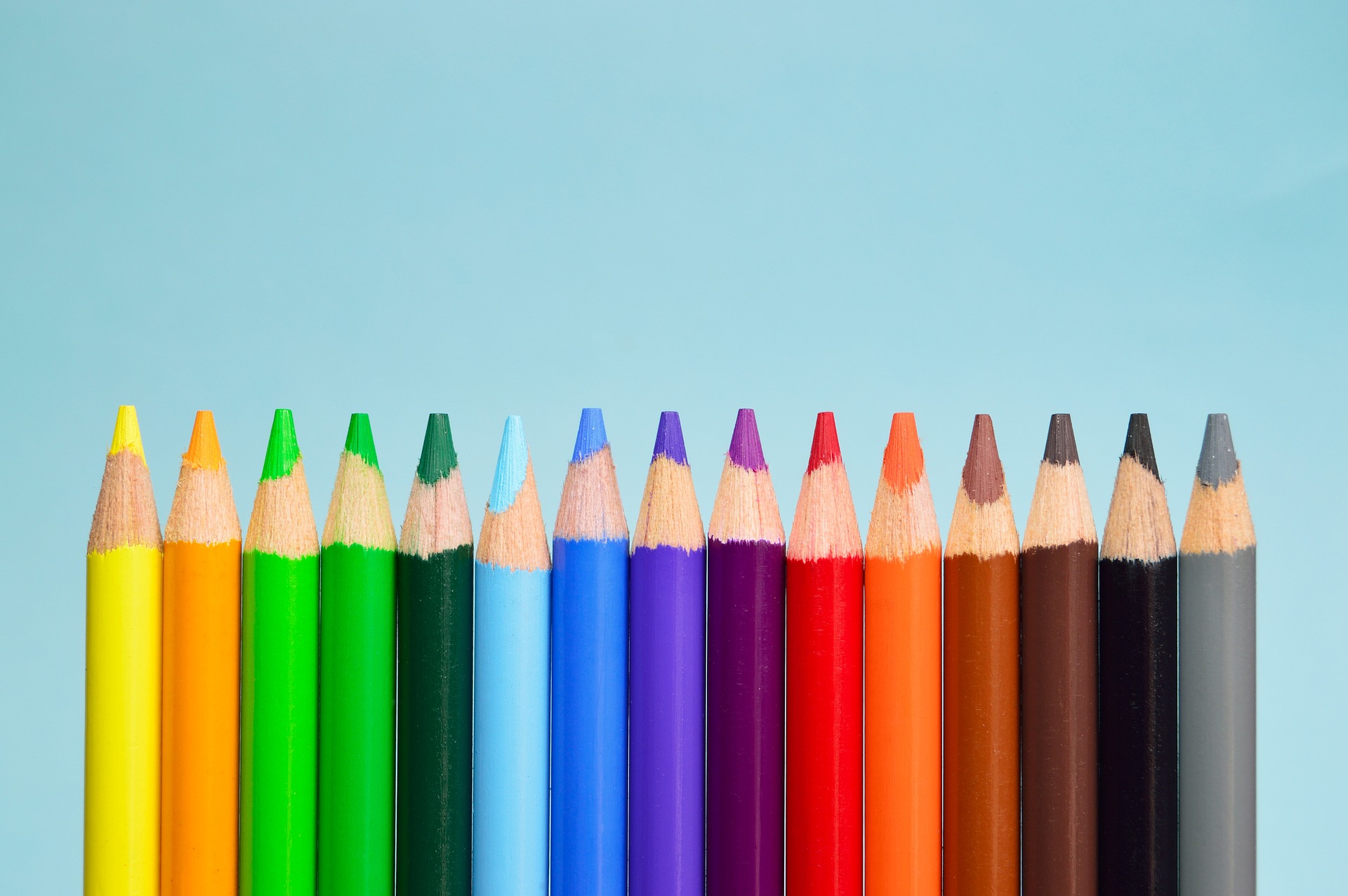 Colored pencils lined up against a light blue background. 