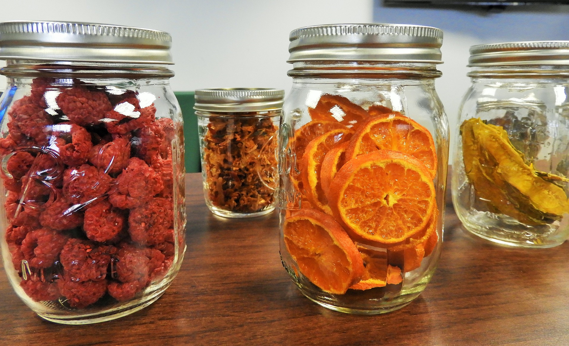 sealed mason jars full of dehydrated produce including a jar of raspberries and one of orange slices