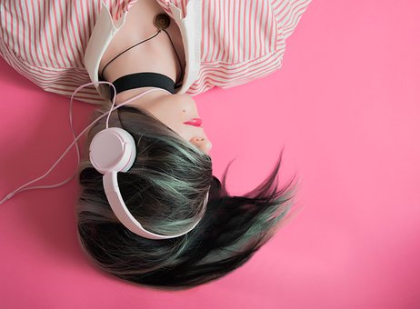 Person with dark hair with headphones on a pink background.