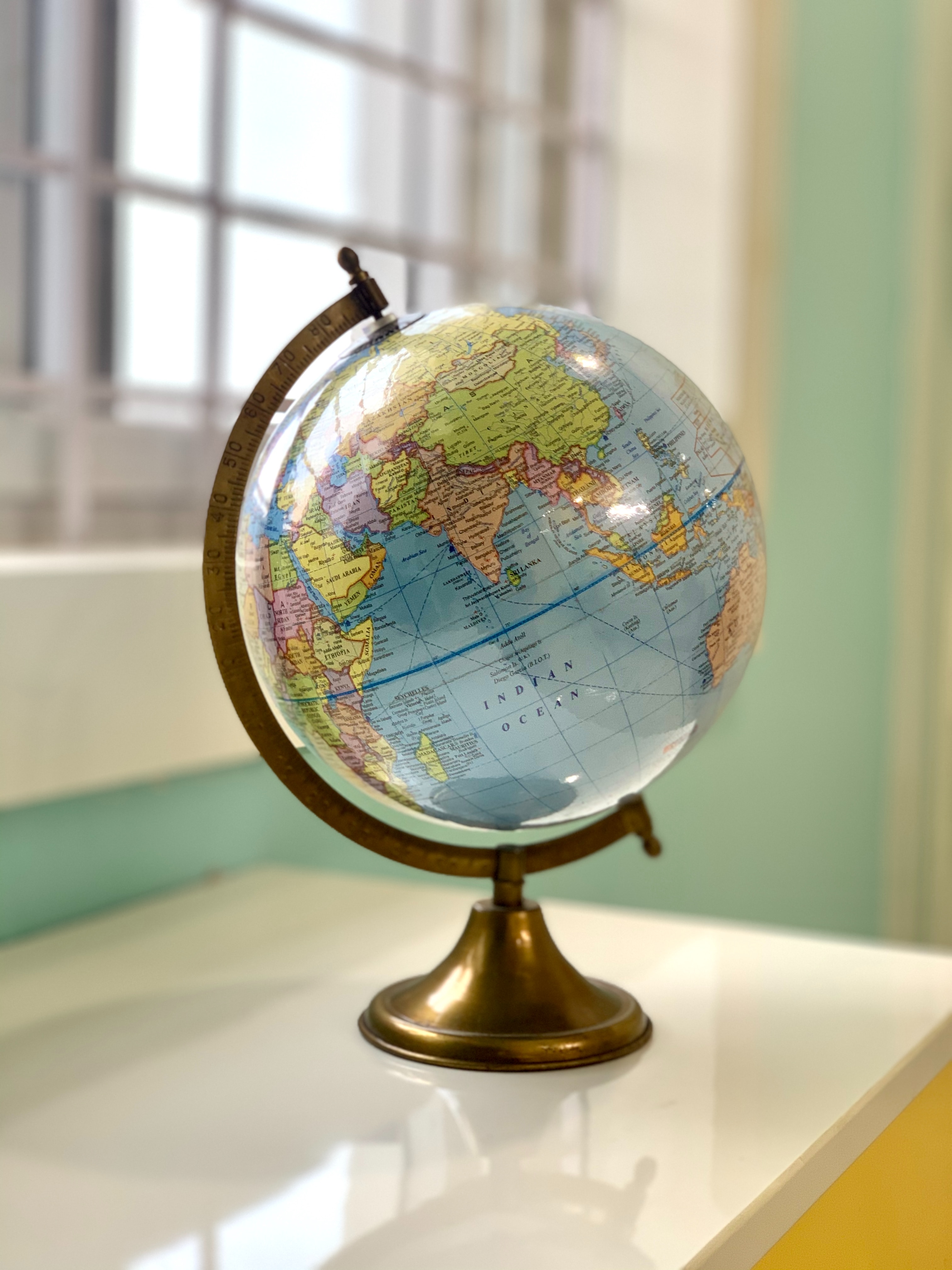 globe on stand sitting on a flat, shiny white surface in front of a white-framed window in a pale teal wall