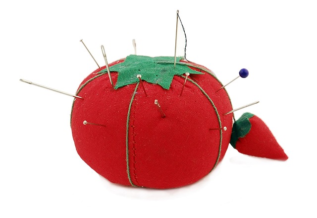 Red pin cushion that looks like a tomato with pins and needles stuck in it. 