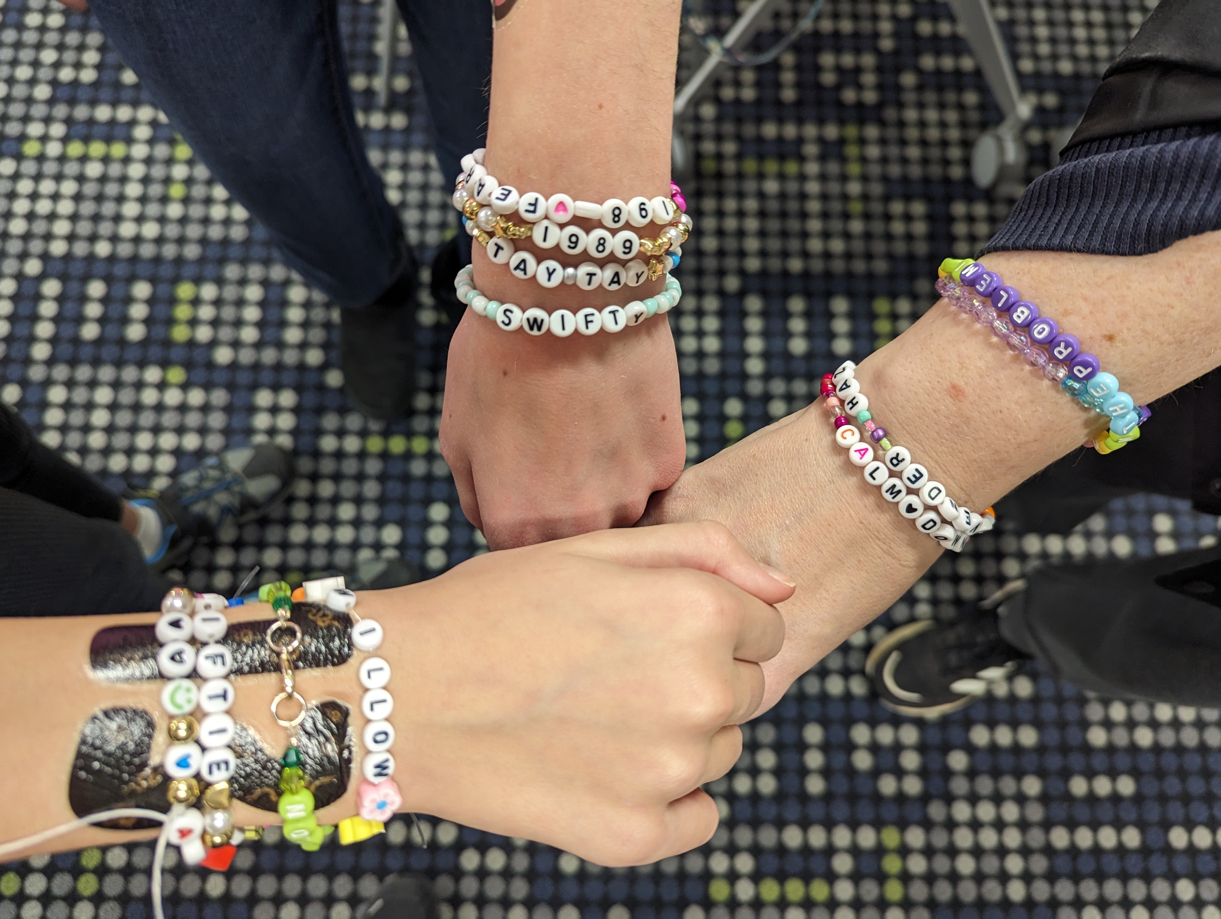 three wrists adorned with colorful Taylor Swift-themed friendship bracelets