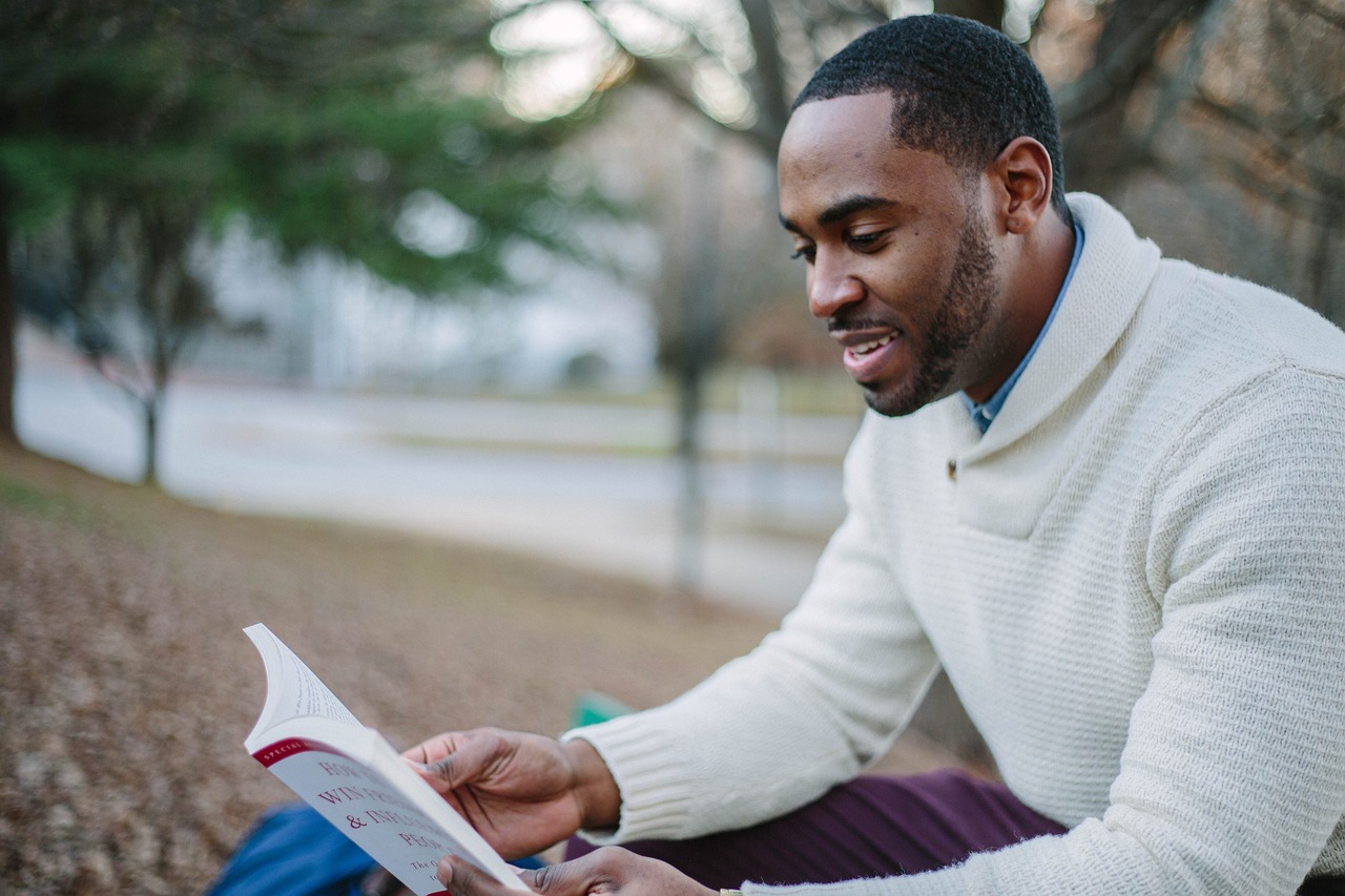 Young man reading a book sitting outside.