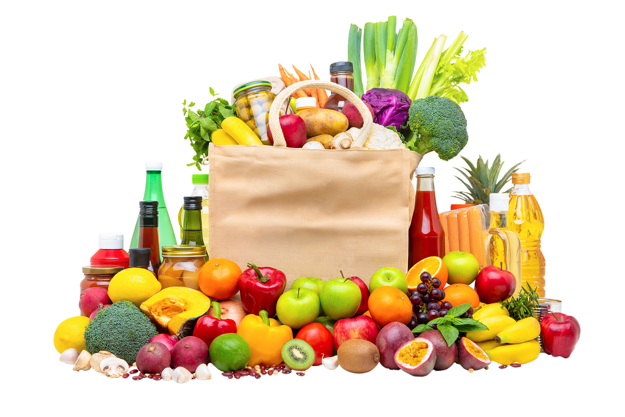 An overflowing bag of groceries, surrounded by a wide variety of fruit and vegetables.