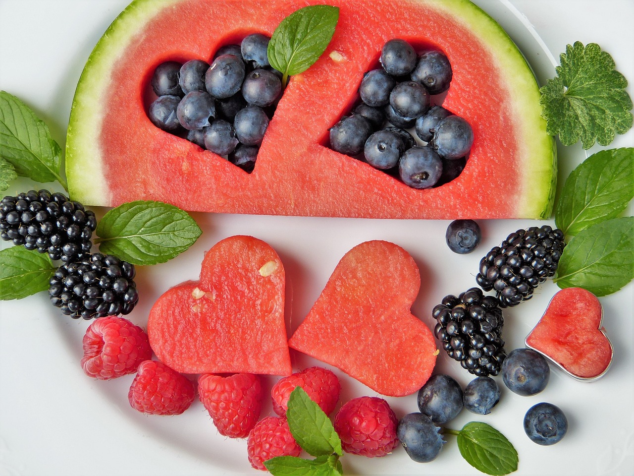A variety of fresh fruit arranged on a plate. Some cut in the shape of a heart.