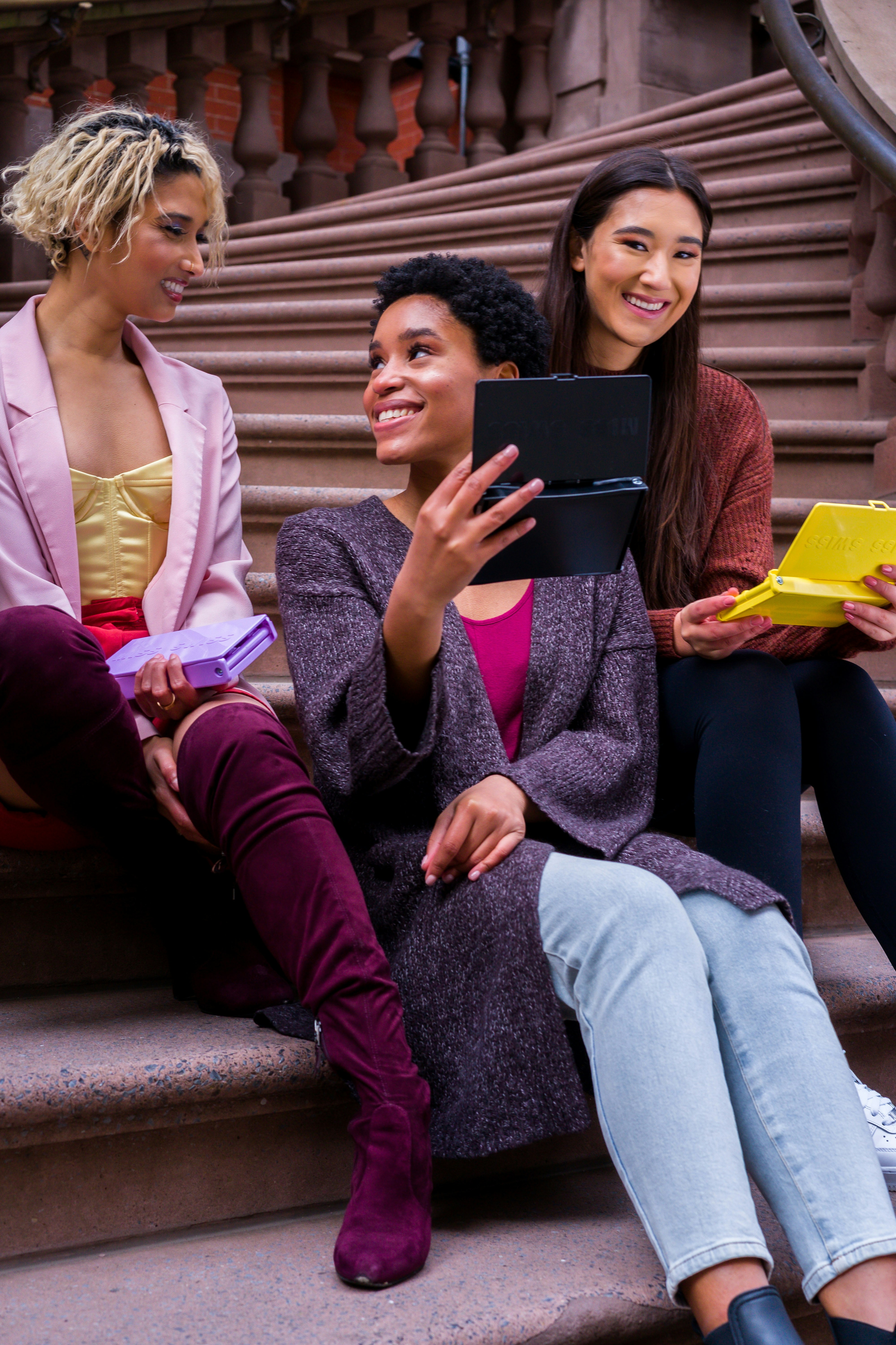 3 women sitting on steps having a discussion about items on their devices.