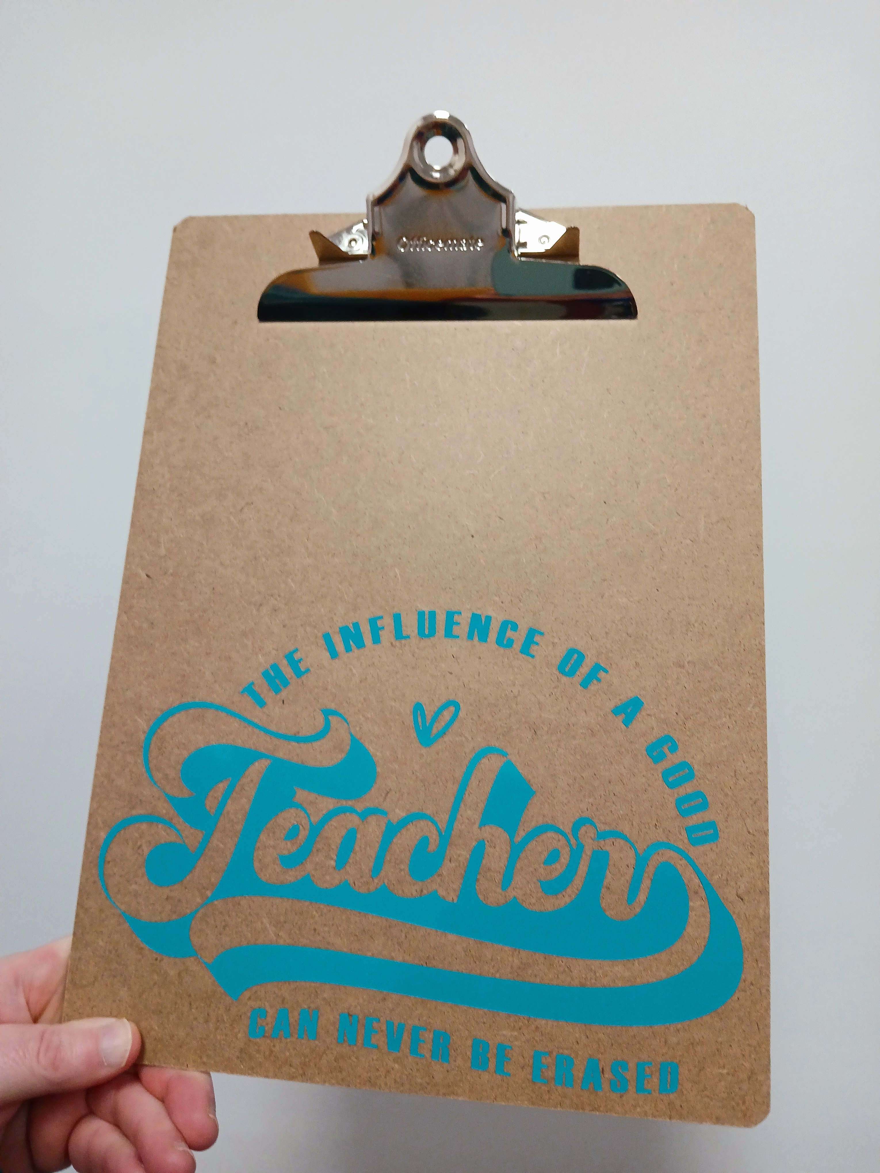 Brown clipboard with teal wording: The influence of a good teacher can never be erased.