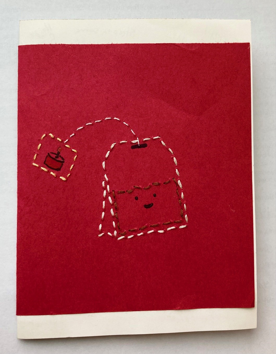 a card of red craftpaper over white cardstock sewn with thread in the outline of a teabag