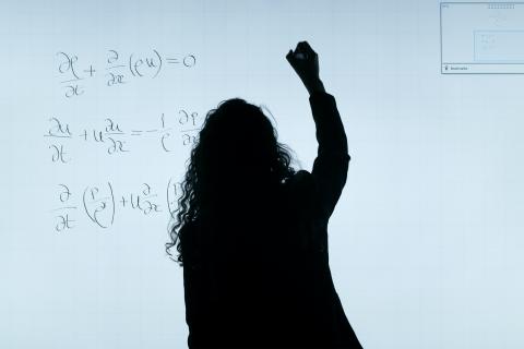 Silouette of a woman writing a math equation on a white board