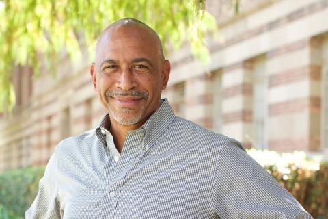 photo of Noguera in a checked shirt standing in front of a blurred out brick building