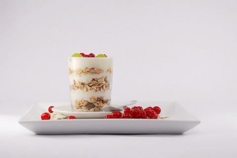 This image shows a rectangular plate with cranberries and a a cup of granola and fruit parfait with a spoon laid next to it.