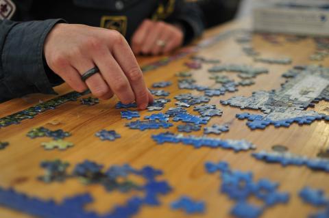 A person's hands working on a jigsaw puzzle on a wooden table