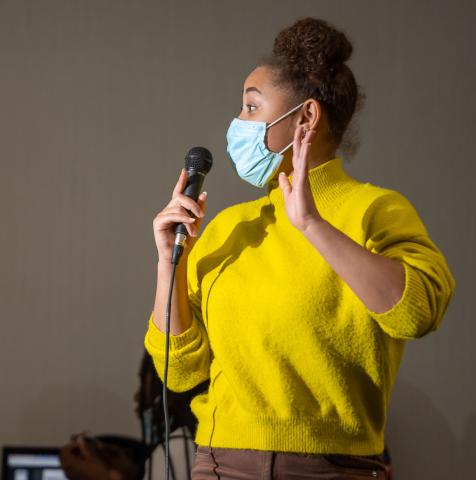 young woman wearing bright yellow sweater holding a microphone