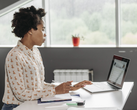 Woman using a laptop at a desk with notebooks.