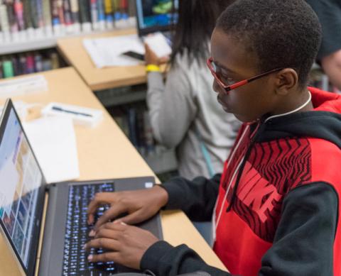 young teen in red and black sweatshirt working on a laptop computer