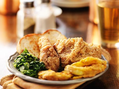 A white plate with collard greens, fried chicken, and eggs arranged in a circle. 