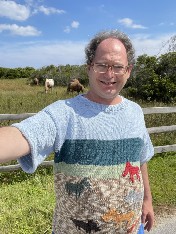 Sam Barsky, standing near horses on Assateague Island, wearing his "Assateague" sweater.