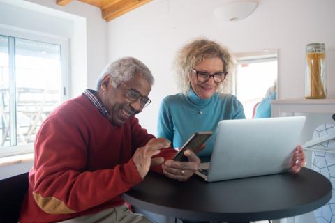 A man and woman smiling while using a cell phone and laptop