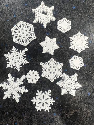 white 3D printed snowflakes of varying shapes on a black speckled background